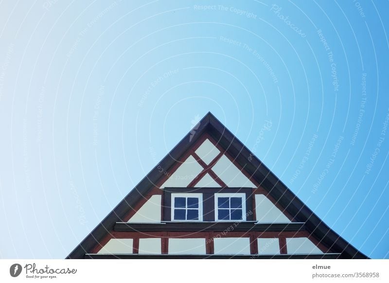 Gable of a renovated half-timbered house with two windows and blue colour gradient in the sky Half-timbered house Triangle pediment Window Blue Color gradient