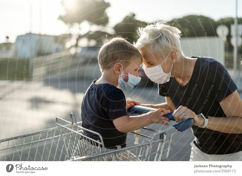 Mother joyfully playing with kid sitting in shopping cart. Both wearing protective face mask. woman mother baby child consumer corona coronavirus happy young