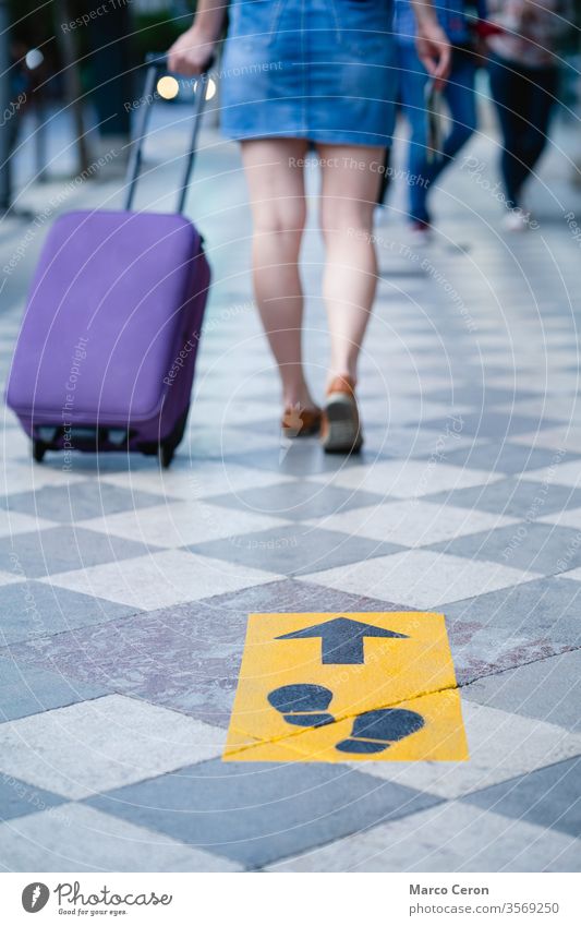 tourist with suitcase walking on a city street marked with social distance safety signs traveller covid-19 label holiday pandemic coronavirus woman