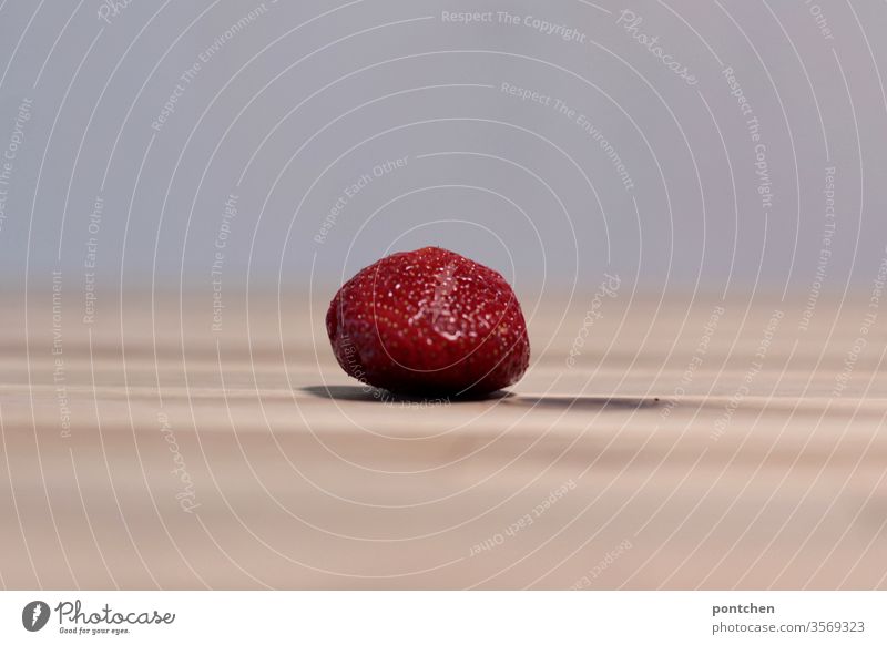 A single strawberry lies on a wooden table and casts a shadow Shadow Healthy Eating fruit vitamins Red Individual Table Nutrition Food Organic produce Delicious