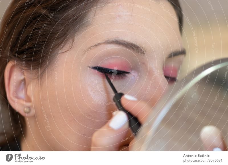 Closeup of an adult brunette aplying eye liner on herself, eyes closed while creating cat eyes health lashes smokey lady brown pretty eyebrow apply beautician