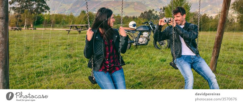 Young man taking a picture of his girlfriend on the swings couple taking picture camera happy motorcycle leather jacket biker banner web panoramic panorama
