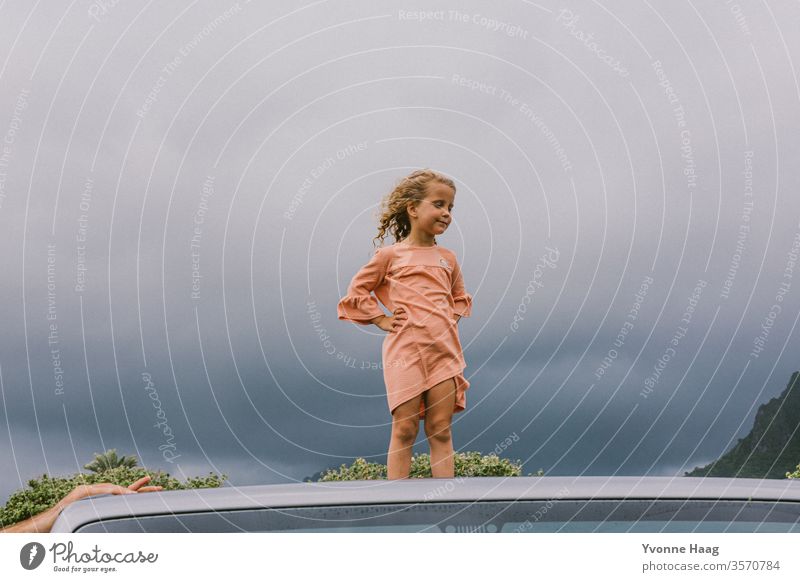 Child stands on the roof of a car and the wind blows her hair back Hawaii Gale Beach Sky Coast Clouds Colour photo Nature Wind Exterior shot Landscape Storm