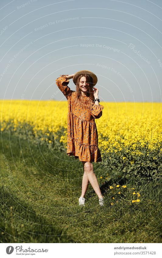stylish young woman in straw hat in a field of yellow flowers. Girl in a floral dress. background with yellow flowers and blue sky girl portrait fashion spring