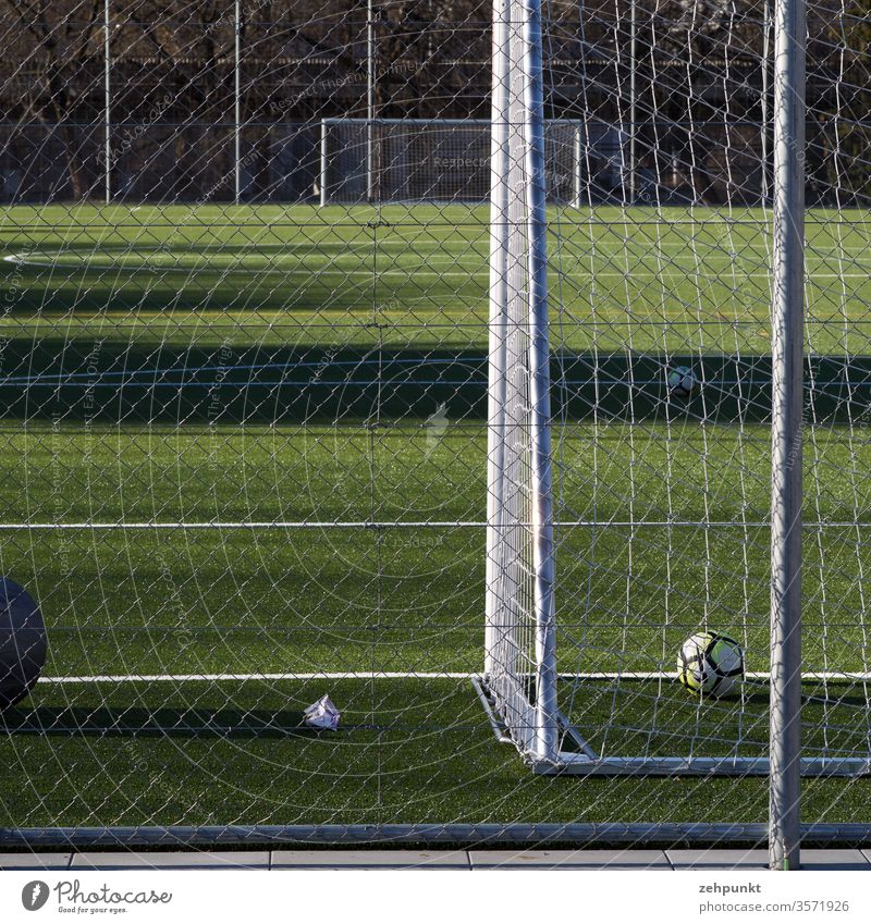 View along the football field from goal to goal. The front goal is cut, a ball is behind the line, wide lateral shadow casts on the field Football pitch