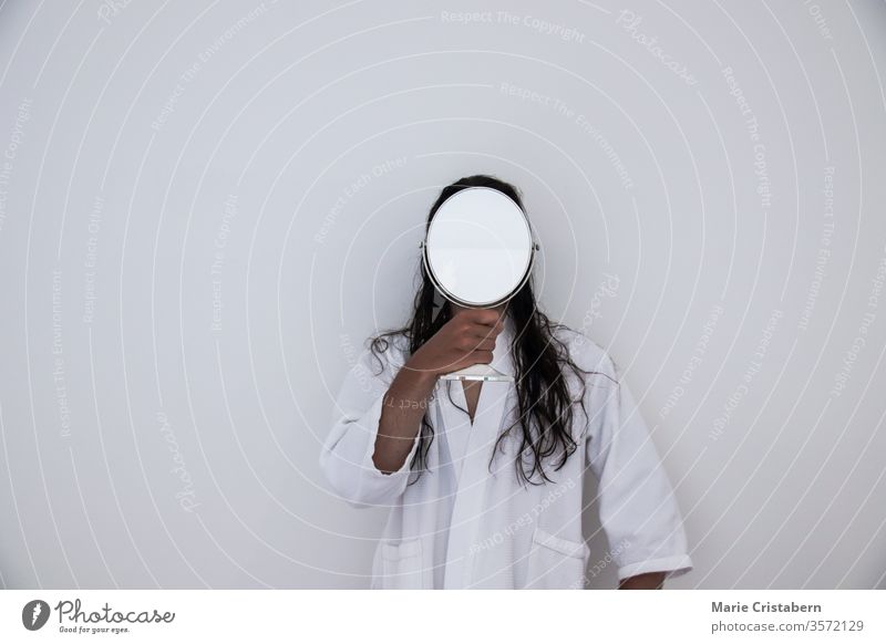 Conceptual photo of a long haired man in white robe holding a mirror in front of his face conceptual image identity concept anonymity mysteriousness