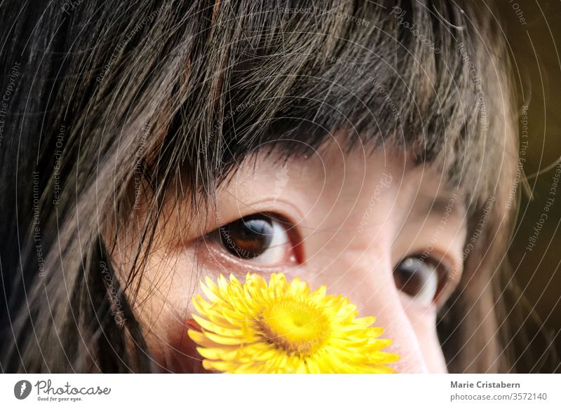Close up of a yellow flower on the face of an almond eyed asian girl innocence pureness childhood portrait happy Portrait photograph Colour photo expression
