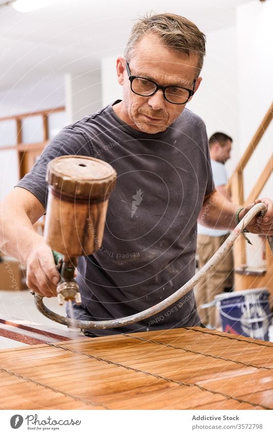 Craftsman applying varnish to wood jalousie using airbrush in carpentry workshop craftsman spray lacquer slats woodwork sprayer tool spray gun wooden airless