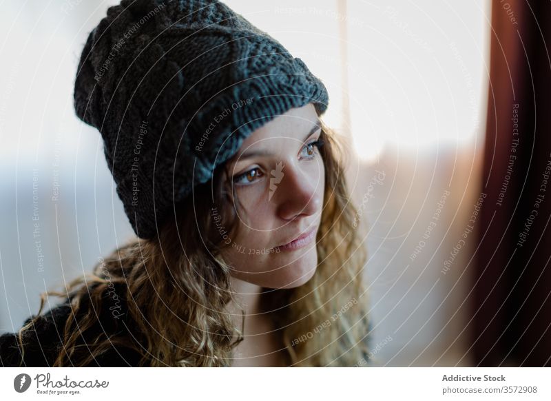 Tranquil young woman in hat looking away with interest and contemplating warm knitted dream melancholy think ponder contemplate watch wait pensive appearance