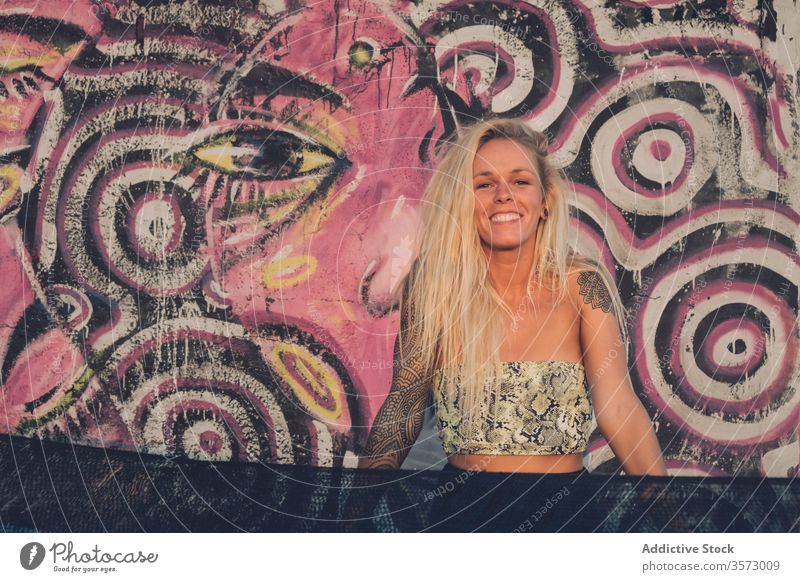 Cheerful young lady standing near wall with colorful graffiti on street woman street style freedom happy summer smile art cheerful urban tattoo positive vivid