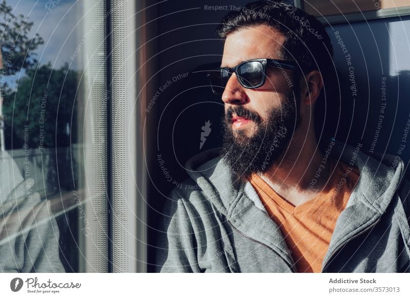 Thoughtful young bearded man looking through window while traveling by train trip dream pensive sunlight summer serious transport passenger seat alone