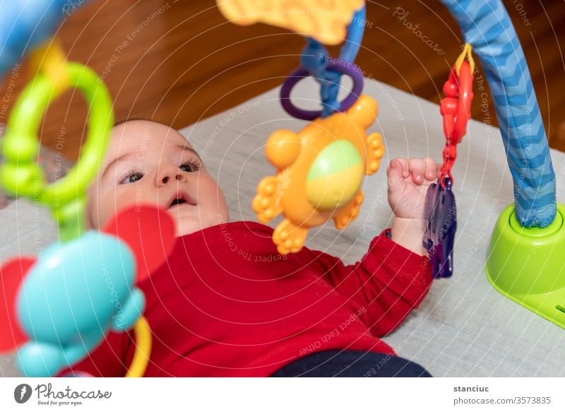 Adorable 6 months old little baby boy on his back surrounded by colourful toys curiosity play enjoyment toddler cute facial expression 6-12 european infant