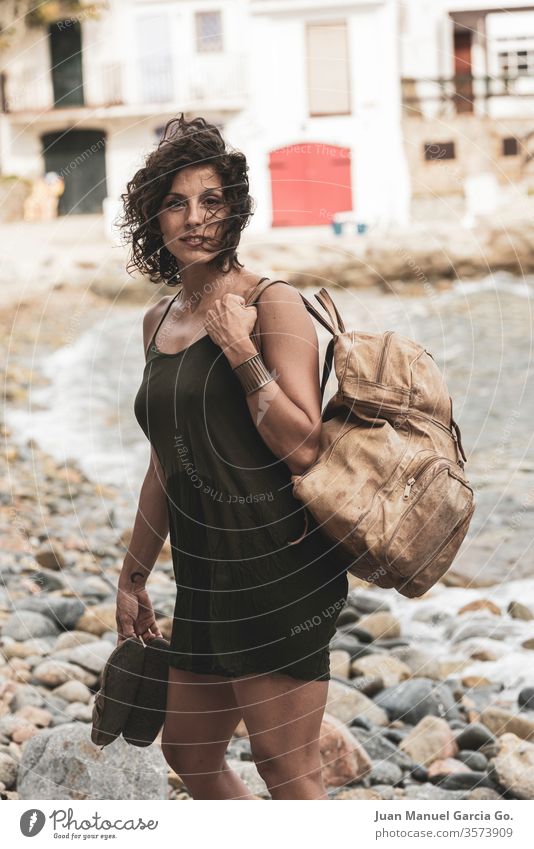 A beautiful female Latina carrying a bag and slippers in the shore