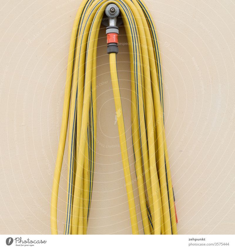 A yellow garden hose is hanging over the tap in front of a beige unstructured wall Garden hose Tap Wall (building) Suspended Hose Yellow minimalism