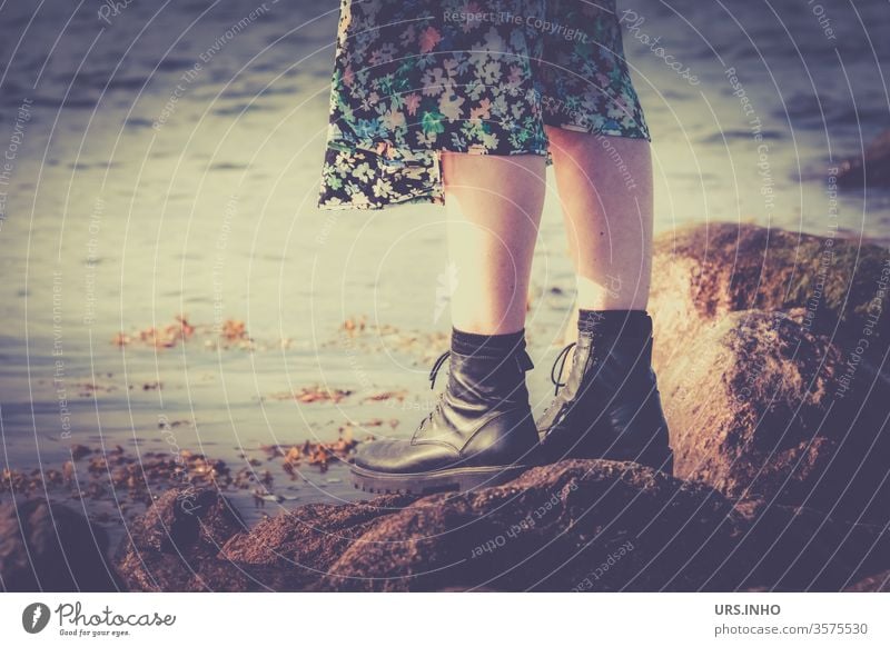 Feet of a woman with boots and flower skirt stand on big stones at the sea Legs vintage Ocean boats Woman Exterior shot Beach natural beach Vacation & Travel