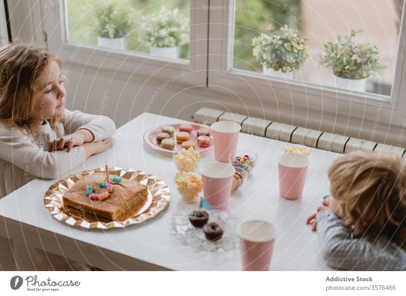 Little kids sitting at table near window in living room children home celebrate birthday cake sibling together garland cozy sweet holiday eat adorable occasion