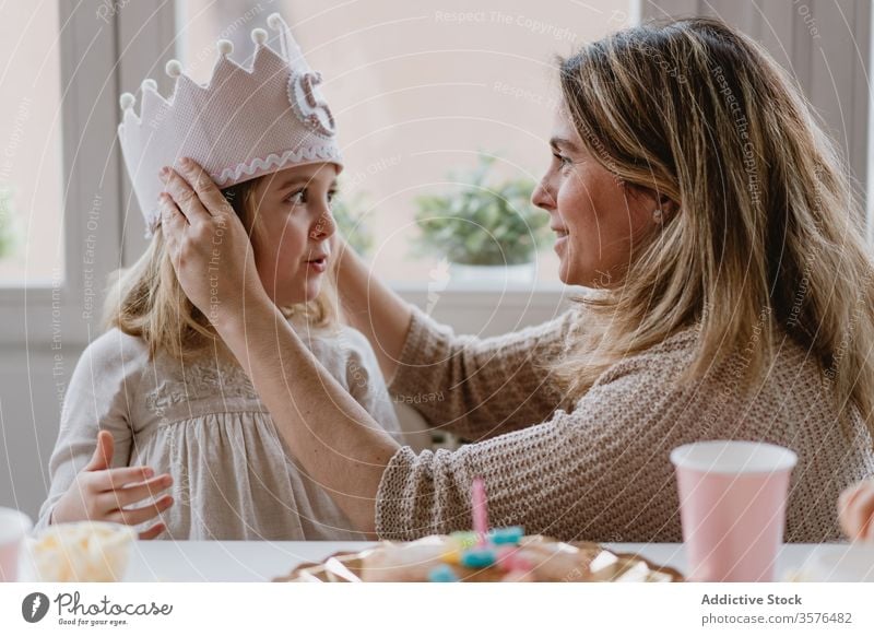 Mother putting decorative  crown on daughter during holiday mother birthday princess love handmade party celebrate home felt kid event fun together girl parent