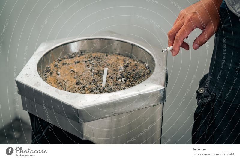 Closeup hand of a man with cigarette. People smoking in smoking zone area of the mall and left cigarette in ashtray. Quit smoke or smoking cessation and lung cancer. 31 May : World no tobacco day.