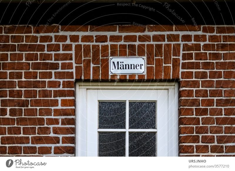 Text on an enamel sign above a door with a muntin window bears the inscription Männer men Lattice window Brick wall Facade lettering Characters Wall (barrier)