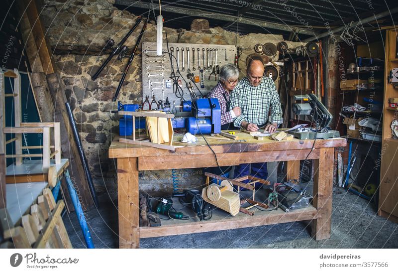 Senior couple in a carpentry workshop work bench senior measures marking working carpenter wood mature machinery business caucasian chair home retirement worker