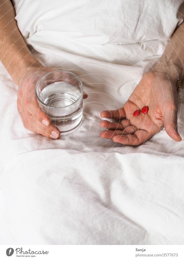 Mann hält ein Glas Wasser und Tabletten in der Hand im Bett krankheit trinkglas coronavirus stay at home Quarantine covid-19 prevention Infection Virus