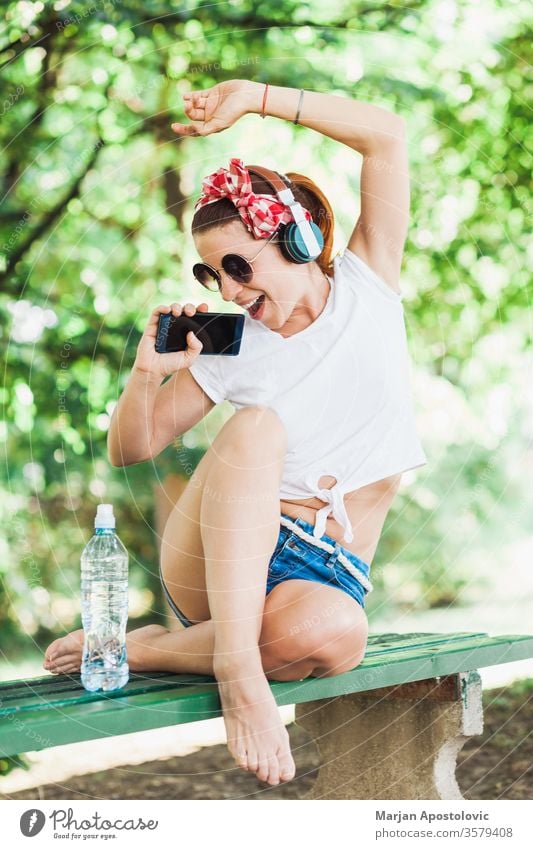 Young woman listening to the music on her smartphone in the park young happy wifi lifestyle enjoying fun joyful singing springtime summer cute beautiful modern