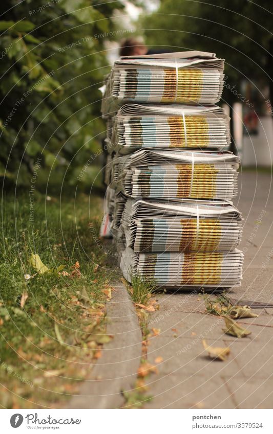 Many stacks of weekly newspapers are standing on the sidewalk waiting to be picked up by the newspaper deliverer. A woman stands bent over them daily newspaper
