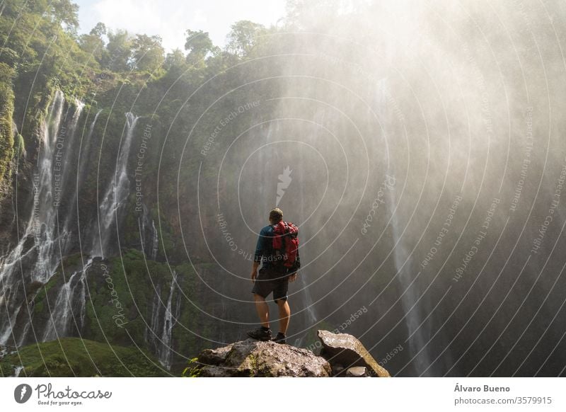 A backpacking adventurer gazes in awe at the massive rock circus formed by the intense waterfalls at Tumpak Sewu in East Java, Indonesia. forest active mountain