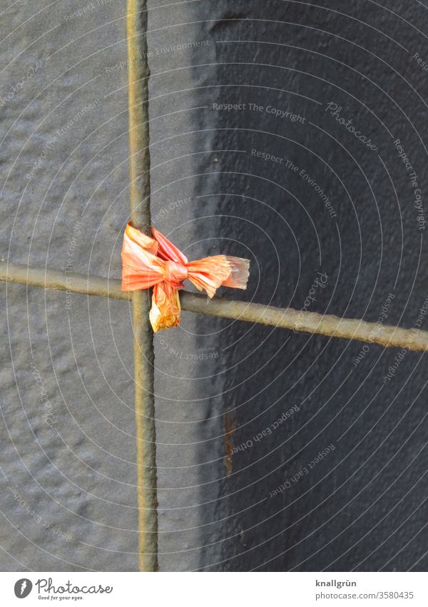 Knotted remainder of an orange fluttering band on a rusty iron bar of a fence in front of a brown background Orange Safety knotted roasted Iron rod Fence
