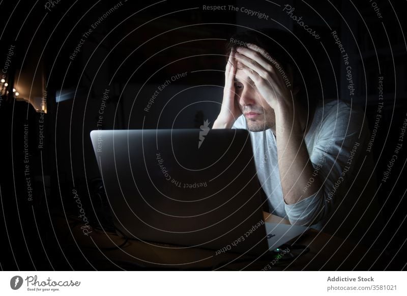Tired man working with laptop at night home tired exhausted online remote dark quarantine stress telework young male casual late device using internet gadget
