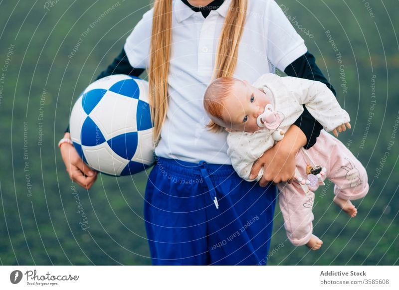 Crop determined girl with soccer ball and doll on field choice football kid stereotype sport child concept uniform game toy training equipment jersey player