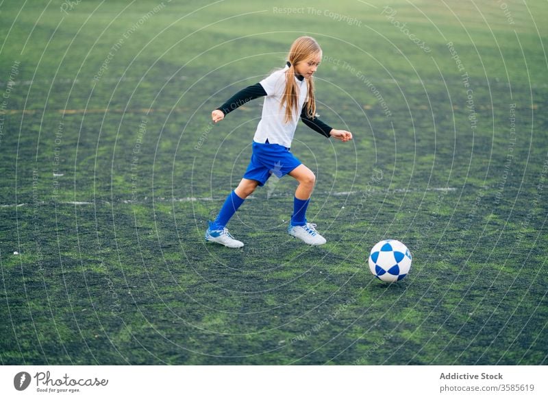 Focused young female player playing football at sports stadium girl soccer field kid run uniform club training child game activity athlete equipment kick