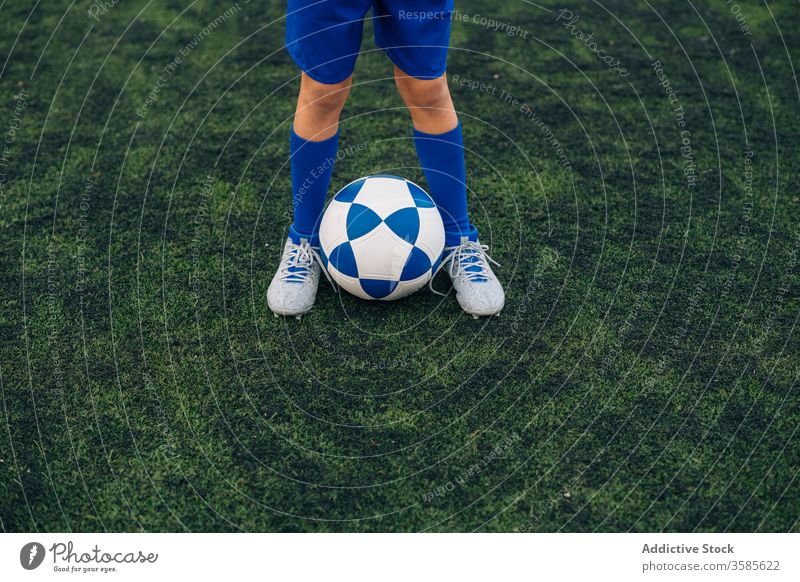 Crop kid in blue uniform with soccer ball on green field in contemporary sports club child football player leg cleats court stadium training athlete jersey game