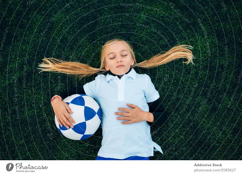 Cheerful girl player with soccer ball relaxing on lawn laugh field football ponytail stadium child kid preteen happy playful optimist uniform equipment sporty