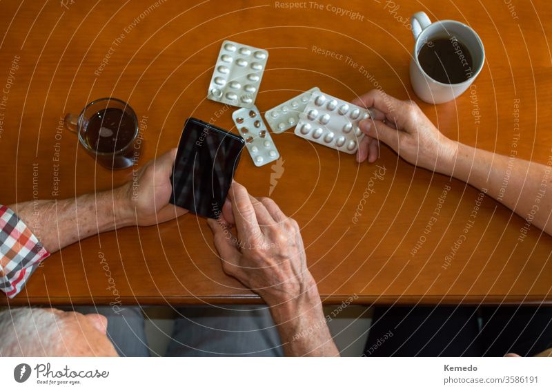 Top views of elderly people using mobile phones to answer medical questions at home while enjoying hot drinks. Old people and use of technology for medical reasons.