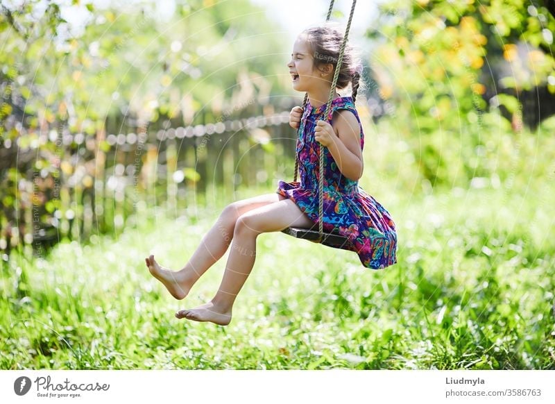 Happy little girl is smiling and  swinging  in the garden in a sunny summer day. laugh funny outdoor smile summertime lifestyle emotions sit tree exercise