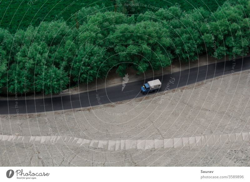 An aerial view of a moving truck on an empty road separated by green trees and the barrens. transportation car truck transportation travel landscape aerial shot