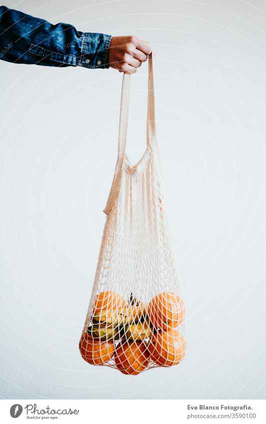 woman han holds a modern shopping bag made of white textile with orange. front view, white background. zero waste concept Orange cotton bag no waste fruits