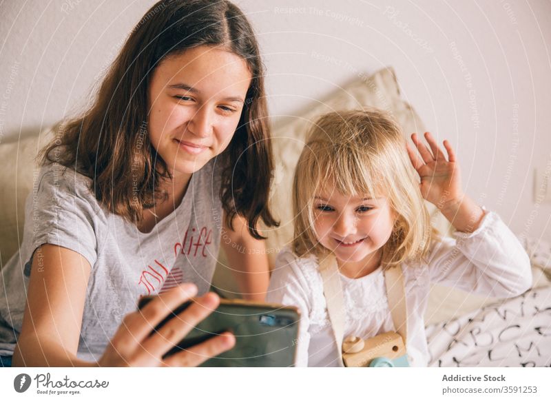 Cheerful sisters taking selfie on smartphone at home grimace girl sibling using having fun gesture teenage little peace charming content camera device gadget