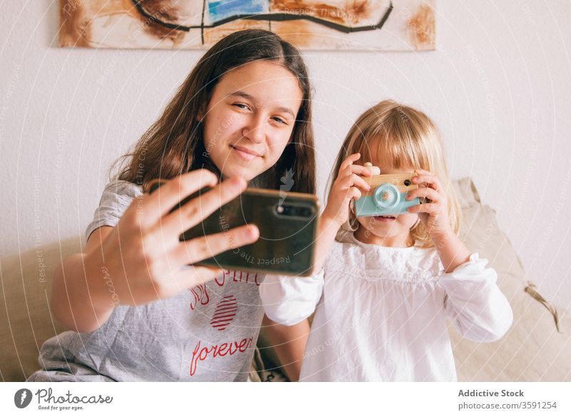 Content sisters taking selfie on mobile phone smartphone teenage little girl using charming content having fun toy camera device gadget kid bed sit adorable