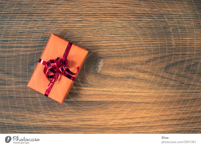 A wrapped gift with a red ribbon on a wooden background Gift Packaging Gift wrapping Birthday Christmas Christmas gift Birthday gift Red Pink Wood Anticipation