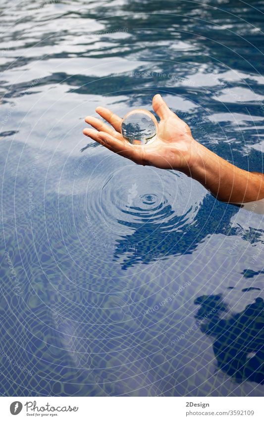 Human hand holding a glass ball over the water transparent crystal ball reflection glasses light vacation medium magic wave gold imagination sphere prophecy