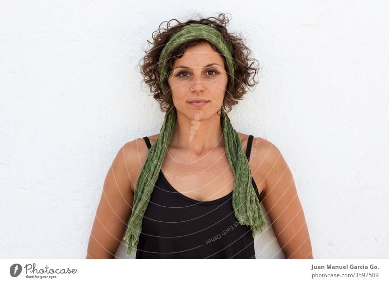 A curly caucasian brunette female with a green hairband standing in front of a white wall with hands behind the back woman person young adult beauty isolated