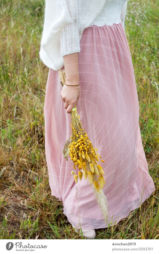 woman is wearing a pink skirt and a white top, above the top is a white light jacket she is holding flowers in her hand Dress Skirt Bouquet Dried flowers Yellow