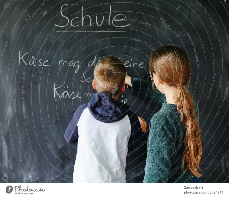 Homeschooling IV - Children play school, one of them writes with chalk on a blackboard a practice sentence for cursive writing School Boy (child) pupil schuler