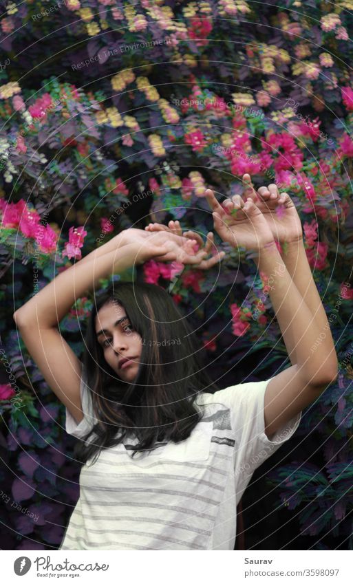Young woman with medium length waving her hands raised up in front of colorful flower bush. Glitch effect. Youth (Young adults) Youth culture