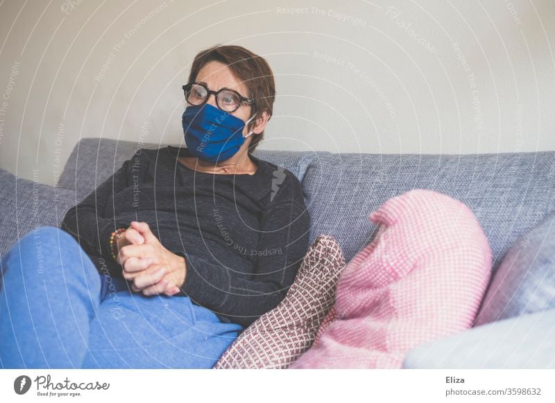 A woman sits on the sofa at home with a mask to protect her from being infected with Corona. Mask Woman Sofa Face mask portrait Sit corona Virus Protection