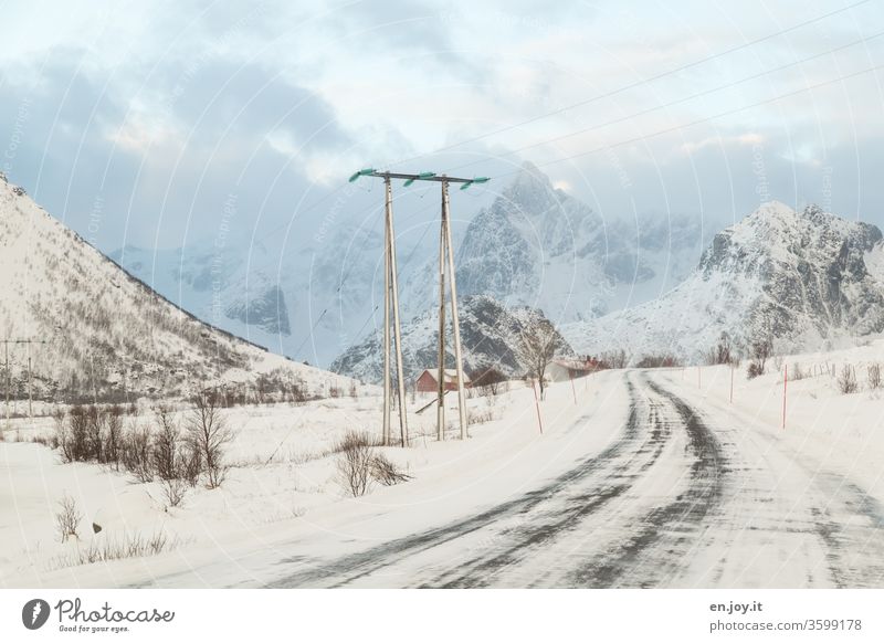 snowy road in Norway leads under a power line in front of mountains with snow Lofotes Scandinavia Winter Snow Street Electricity pylon power supply Climate