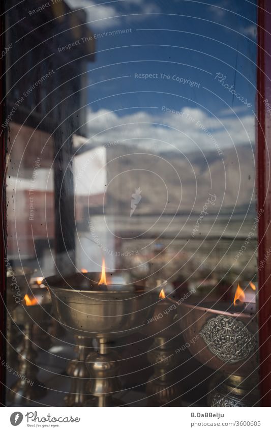 Ancient Tibetan oil lamps behind a window pane reflecting a mountain range of the Himalayas. Rock Nature mountains Valley Tall Colour photo Sky Clouds Landscape