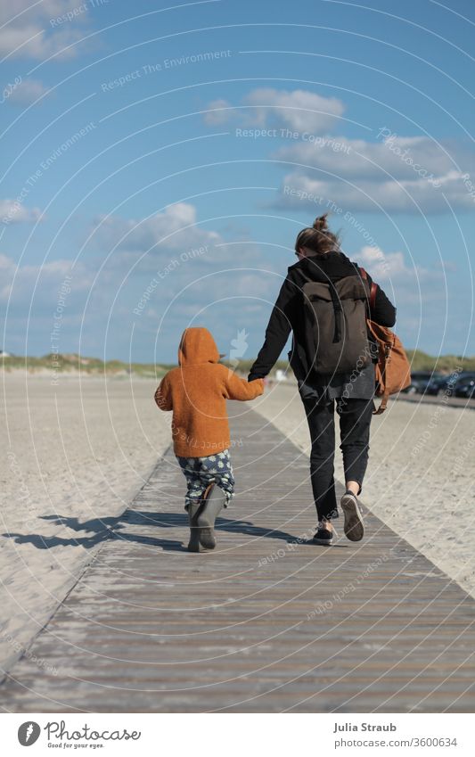 Woman and child walking holding hands on a wooden path to the beach Sand white sand North Sea dunes Marram grass Backpack backpacker Toddler wollwalk